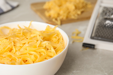 Delicious grated cheese in bowl on grey table, closeup