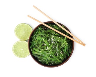 Photo of Tasty seaweed salad in bowl, chopsticks and pieces of lime isolated on white, top view