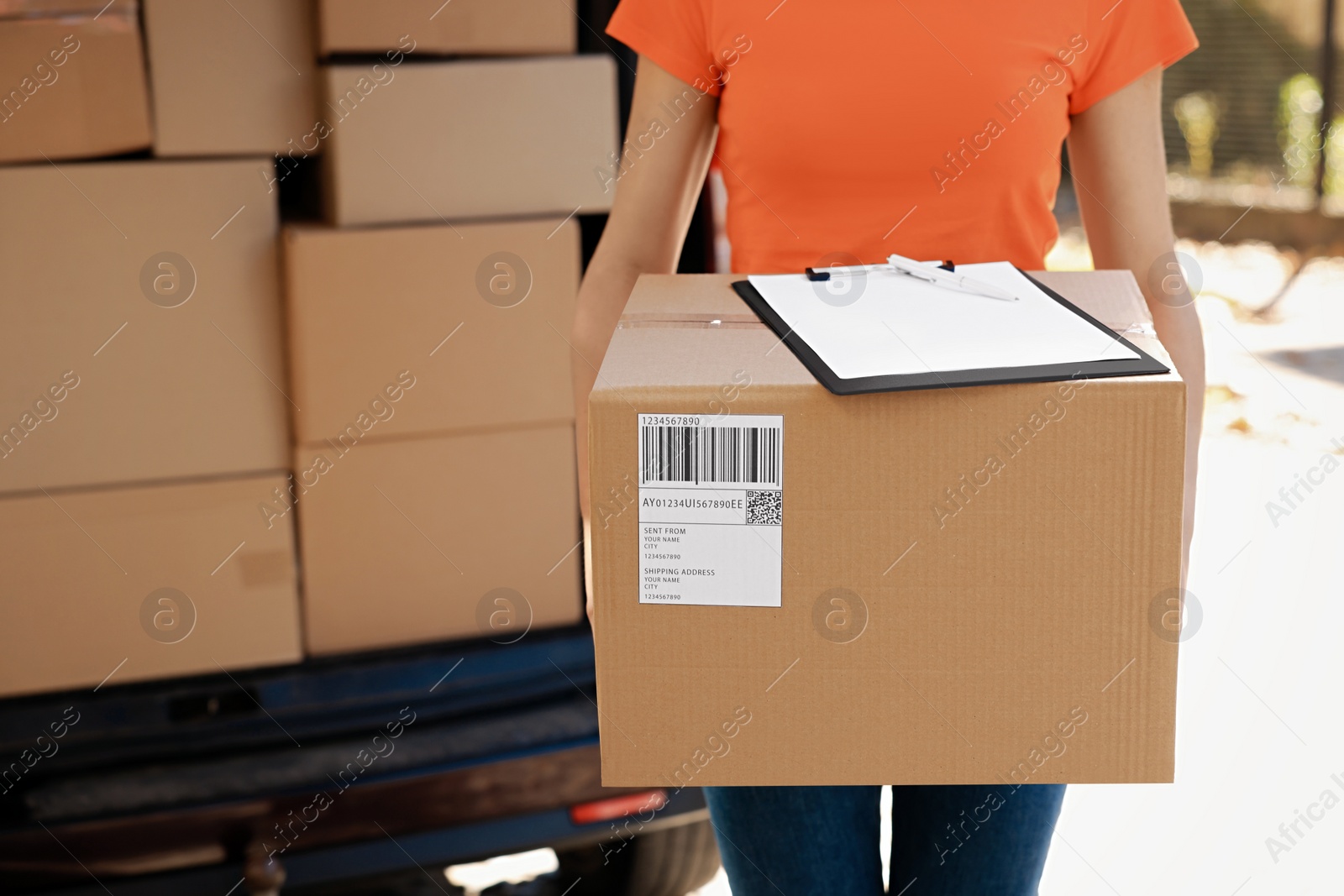 Photo of Courier holding package and clipboard near delivery truck outdoors, closeup