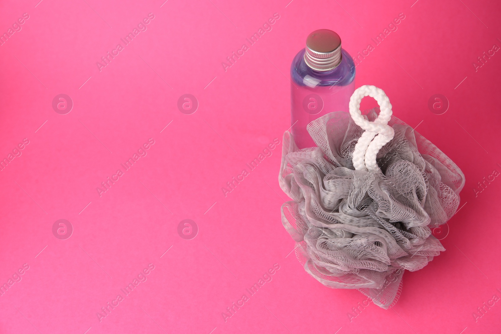 Photo of Grey shower puff and bottle of cosmetic product on pink background, space for text