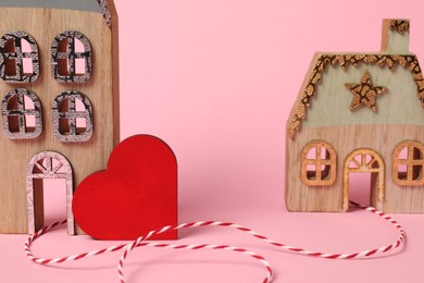 Photo of Decorative heart and cord between two house models on pink background symbolizing connection in long-distance relationship, closeup
