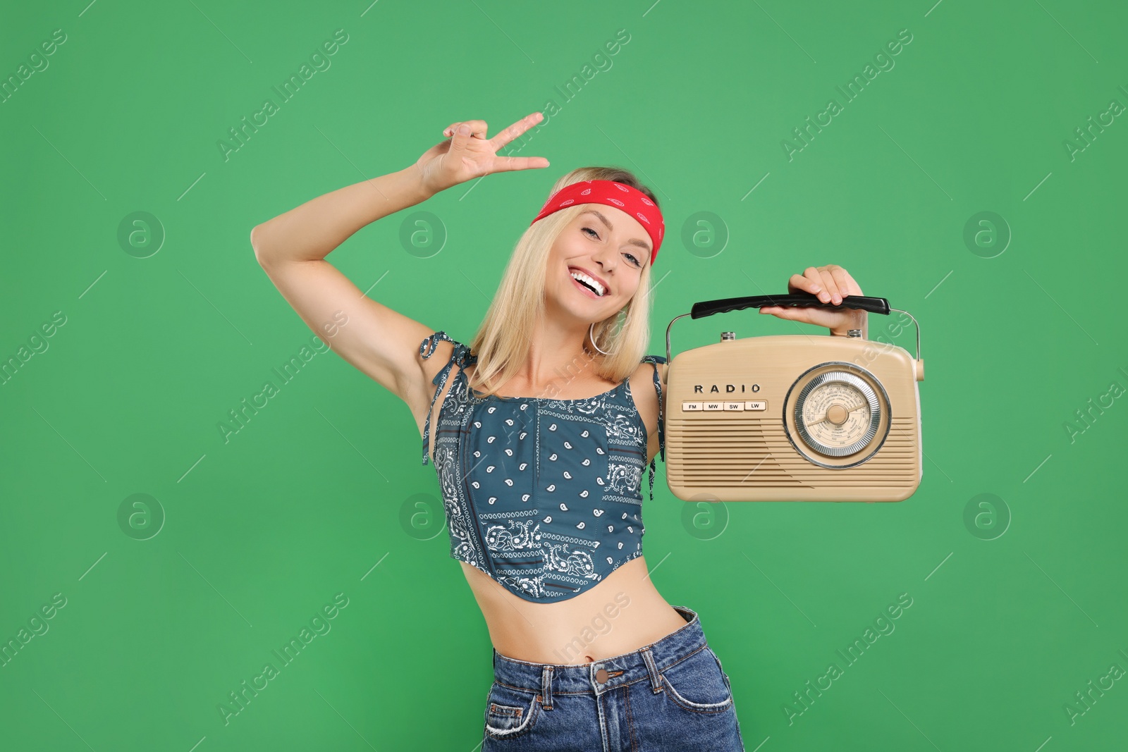 Photo of Happy hippie woman with retro radio receiver showing peace sign on green background