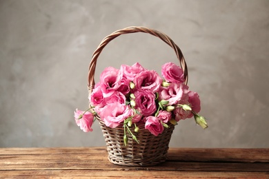 Beautiful pink Eustoma flowers in wicker basket on wooden table against grey background
