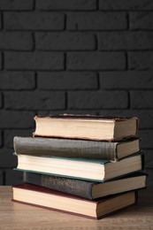 Photo of Stack of old hardcover books on wooden table near black brick wall, space for text