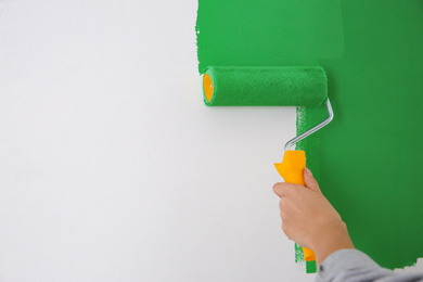 Photo of Woman painting white wall with green dye, closeup. Interior renovation