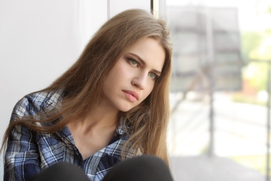 Photo of Depressed young woman sitting near window