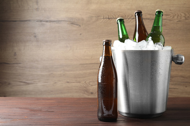 Photo of Metal bucket with beer and ice cubes on wooden table. Space for text