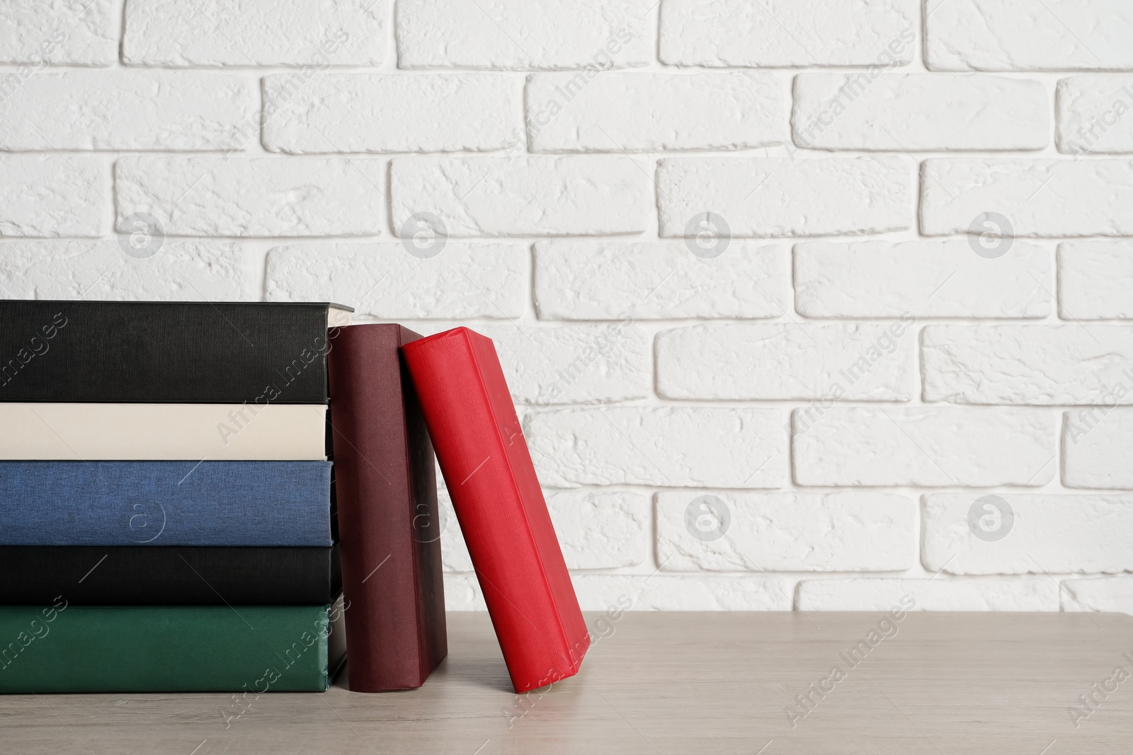 Photo of Many different hardcover books on grey table near white brick wall, space for text