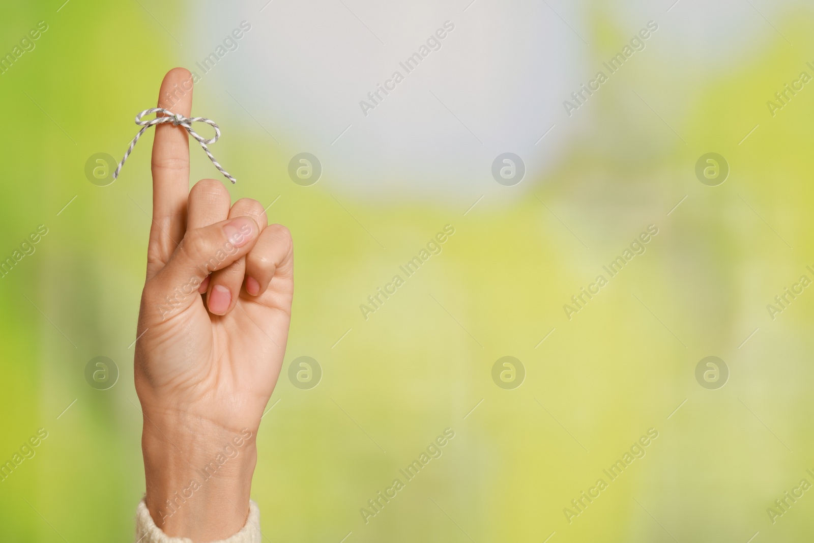 Photo of Woman showing index finger with tied bow as reminder on green blurred background, closeup. Space for text