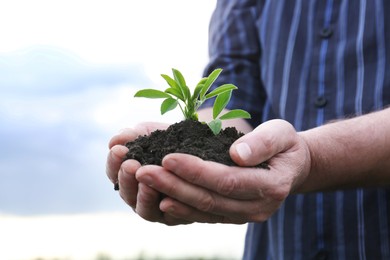 Photo of Man holding pile of soil with seedling against blue sky, closeup