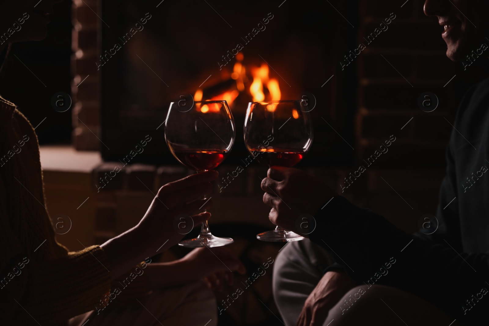 Photo of Couple with glasses of red wine near burning fireplace, closeup