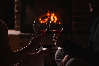 Photo of Couple with glasses of red wine near burning fireplace, closeup