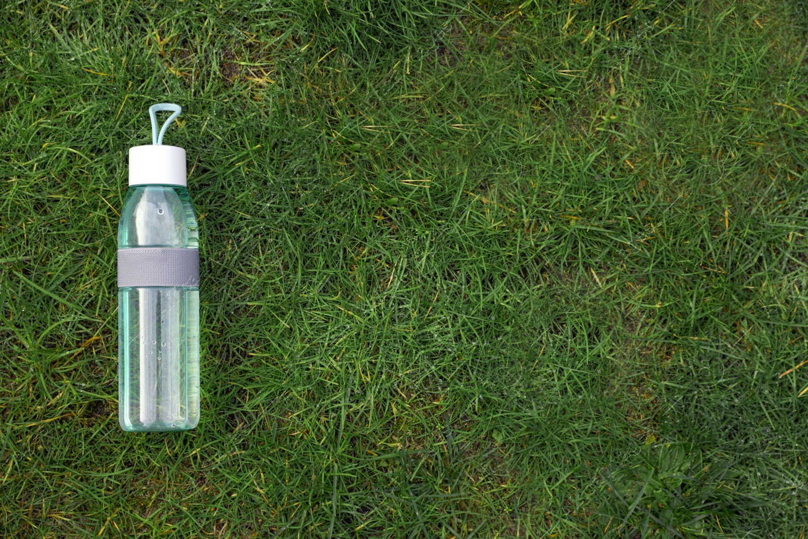 Photo of Bottle of water on green grass, top view with space for text. Morning exercise