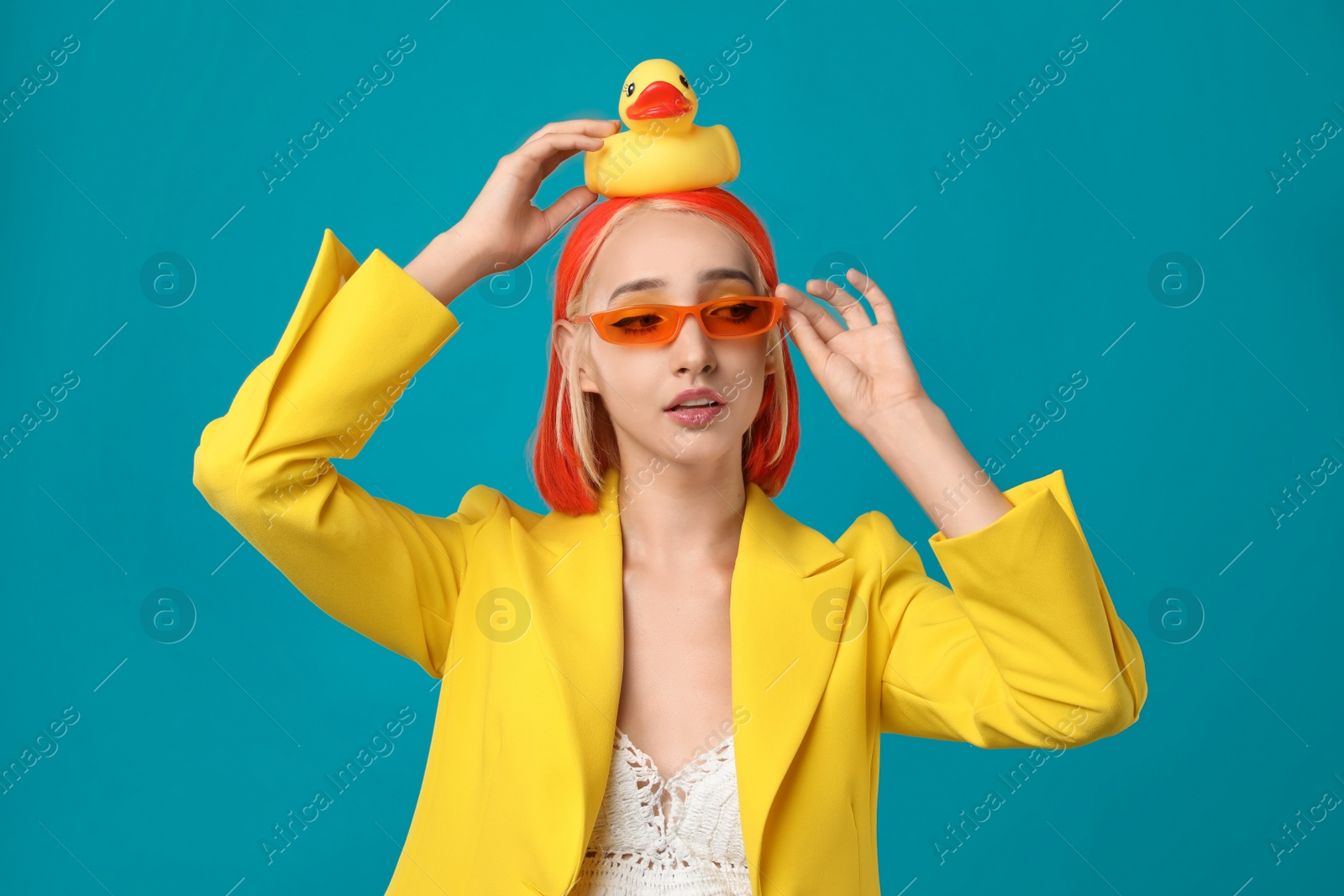 Photo of Beautiful young woman with bright dyed hair and toy duck on turquoise background