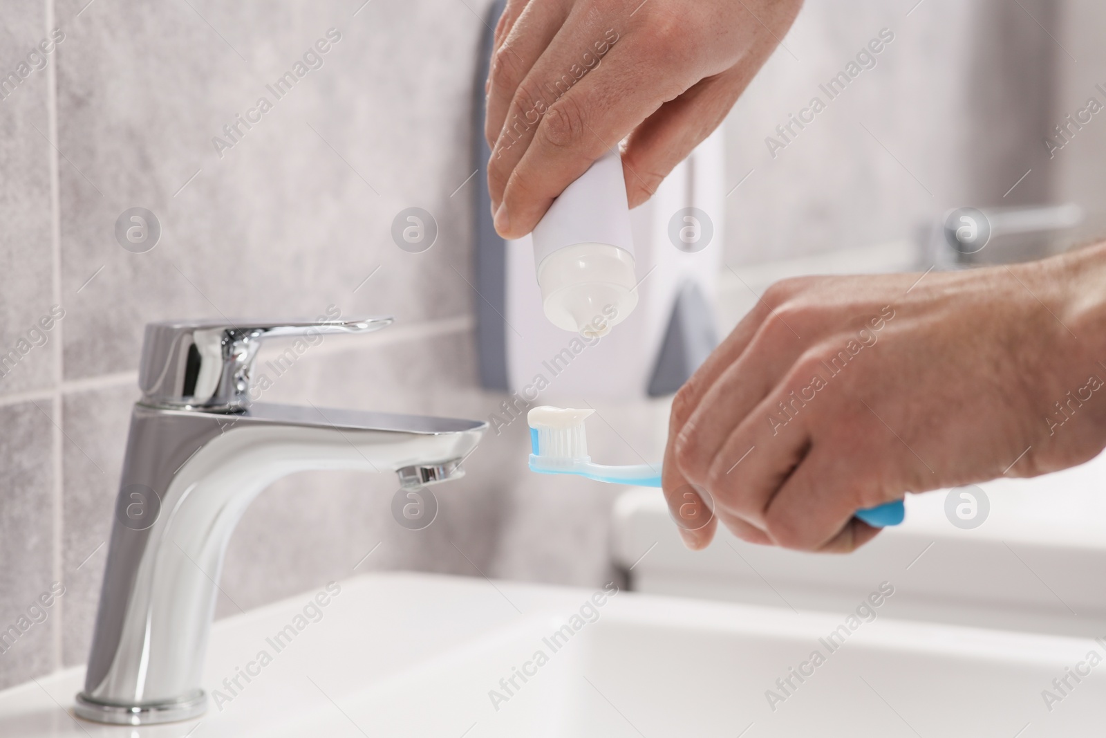 Photo of Man squeezing toothpaste from tube onto toothbrush above sink in bathroom, closeup