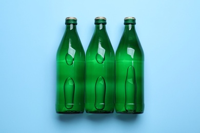 Photo of Glass bottles with water on light blue background, flat lay