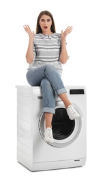 Young woman sitting on washing machine against white background. Laundry equipment