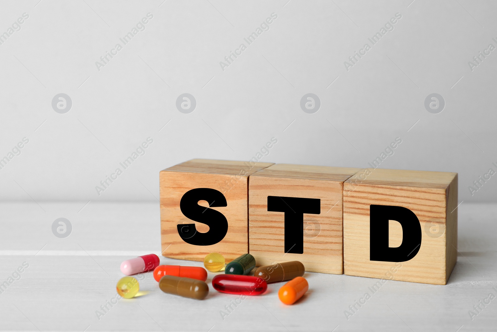 Photo of Abbreviation STD made with cubes near pills on white wooden table