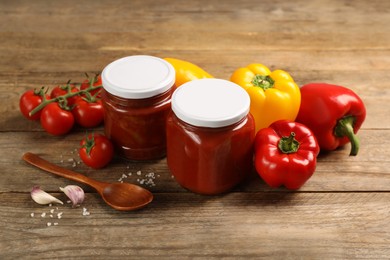 Photo of Glass jars of delicious canned lecho and fresh ingredients on wooden table