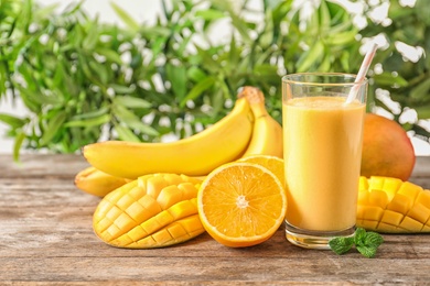 Photo of Fresh tropical drink with ripe mango, orange and banana on wooden table against blurred background