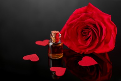 Photo of Bottle of love potion, paper hearts and red rose on mirror surface