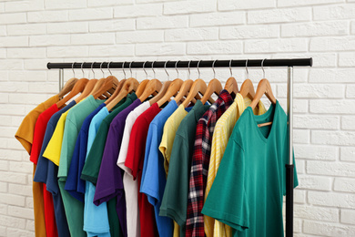 Rack with stylish clothes near white brick wall