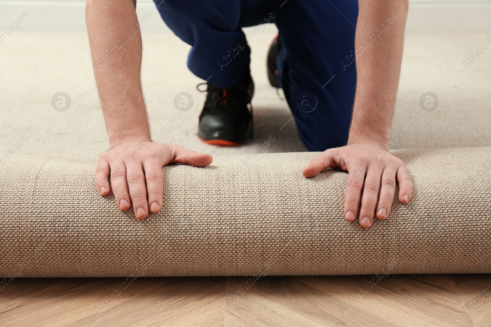 Photo of Worker rolling out new carpet flooring indoors, closeup