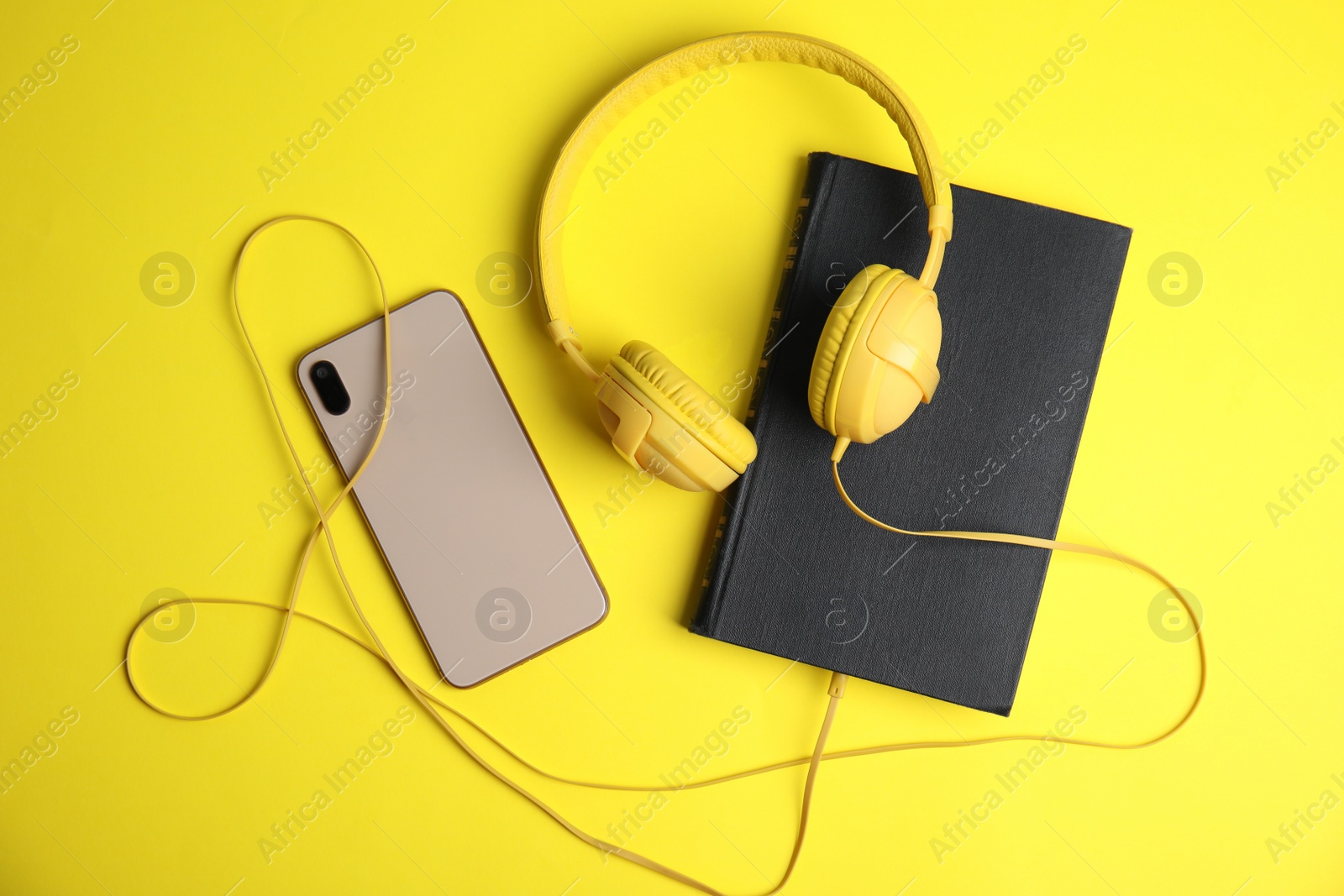 Photo of Book, modern headphones and smartphone on yellow background, flat lay