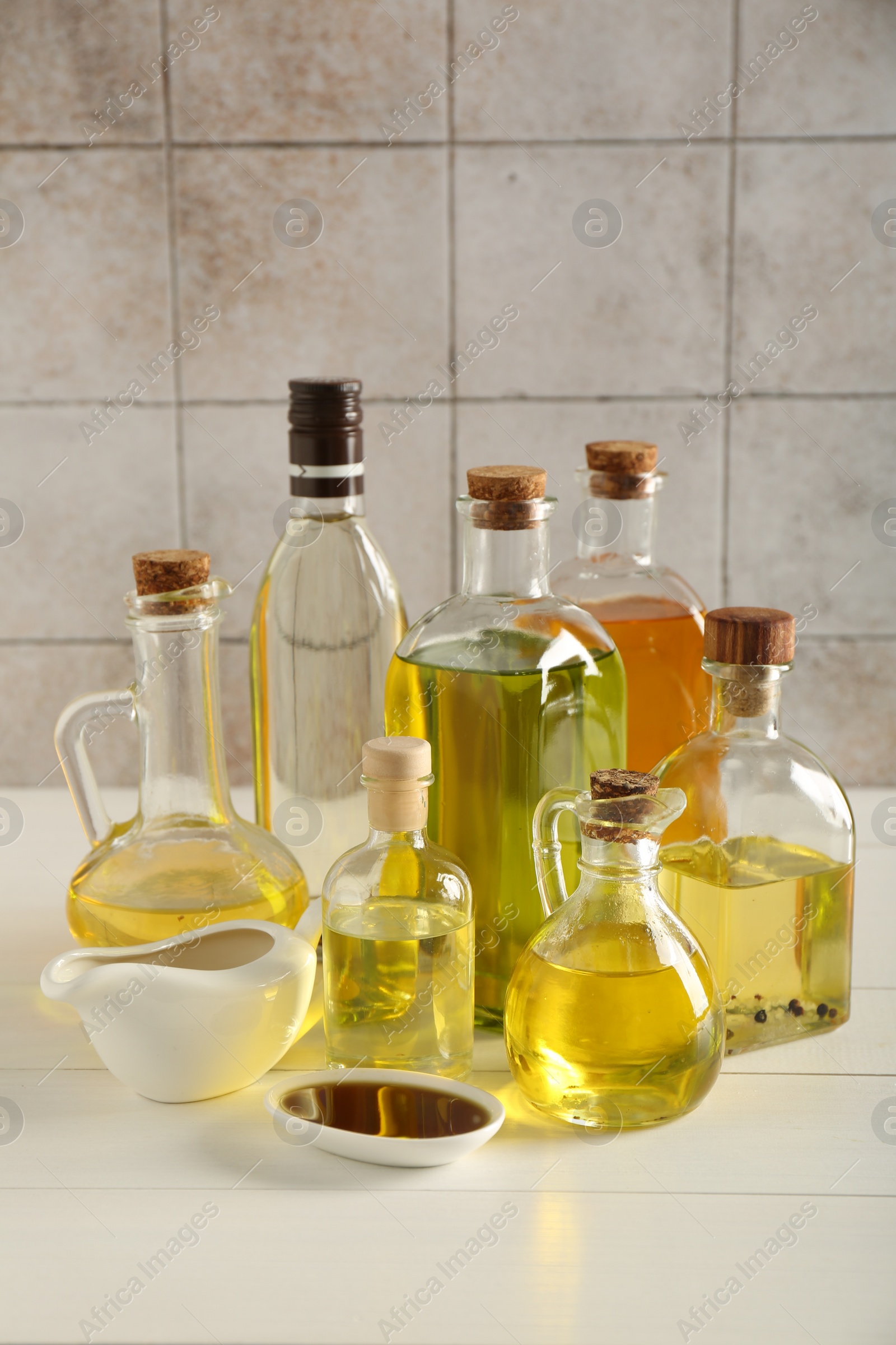 Photo of Vegetable fats. Different oils in glass bottles and dishware on white wooden table against tiled wall