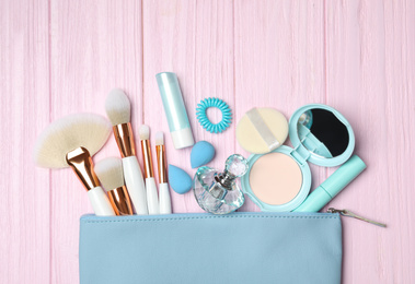 Cosmetic bag with makeup products and beauty accessories on pink wooden background, flat lay