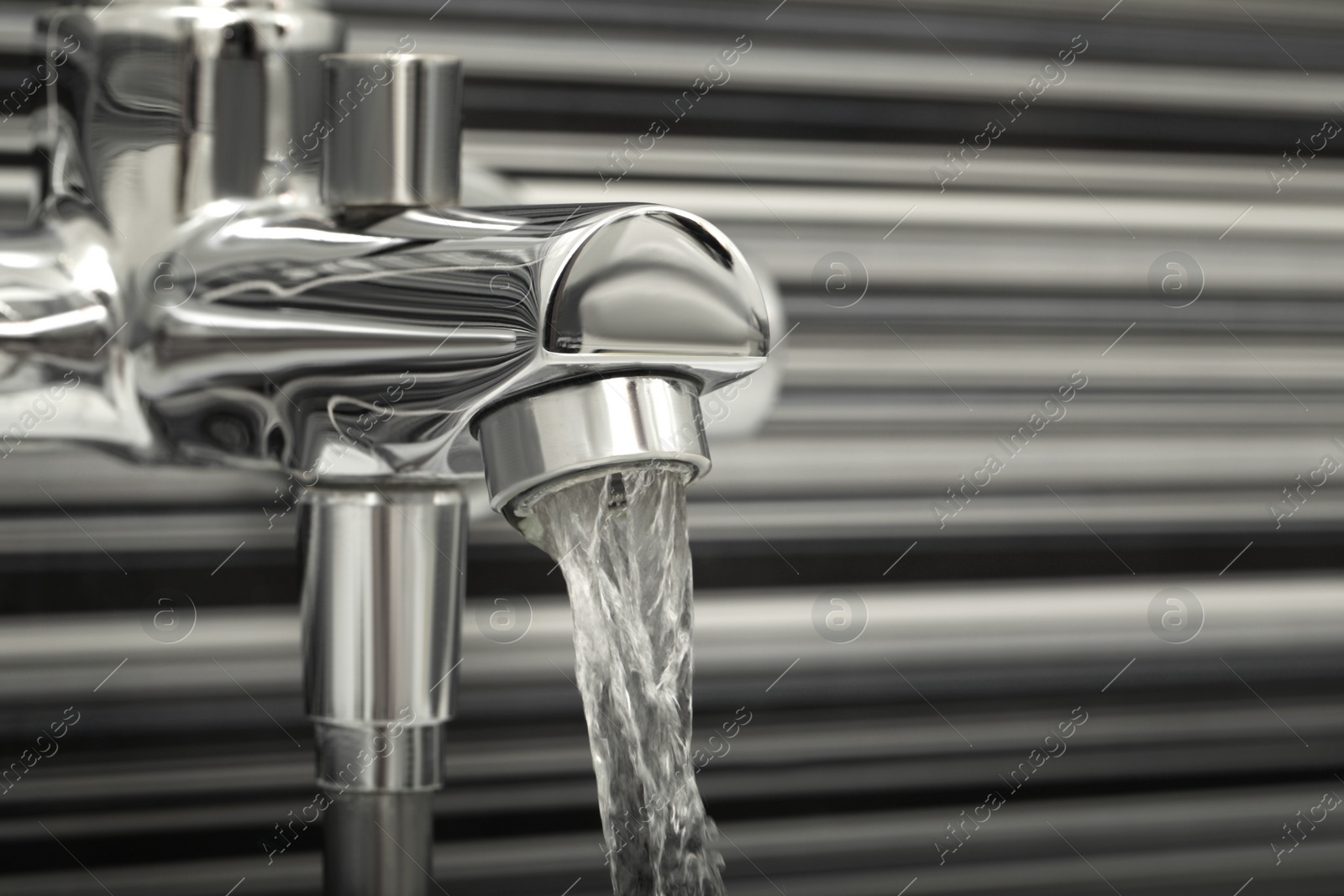 Photo of Water flowing from bath tap on blurred background, closeup