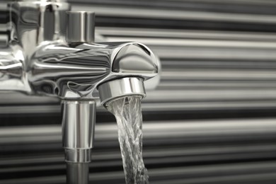 Photo of Water flowing from bath tap on blurred background, closeup