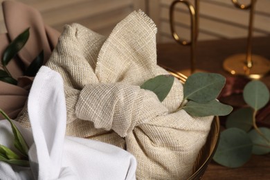 Photo of Furoshiki technique. Gifts packed in different fabrics and eucalyptus leaves on table, closeup