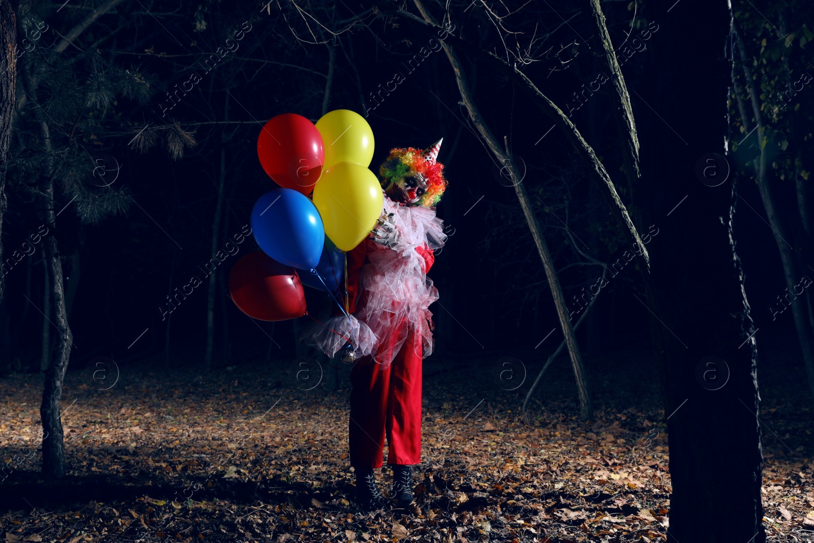 Photo of Terrifying clown with air balloons outdoors at night. Halloween party costume