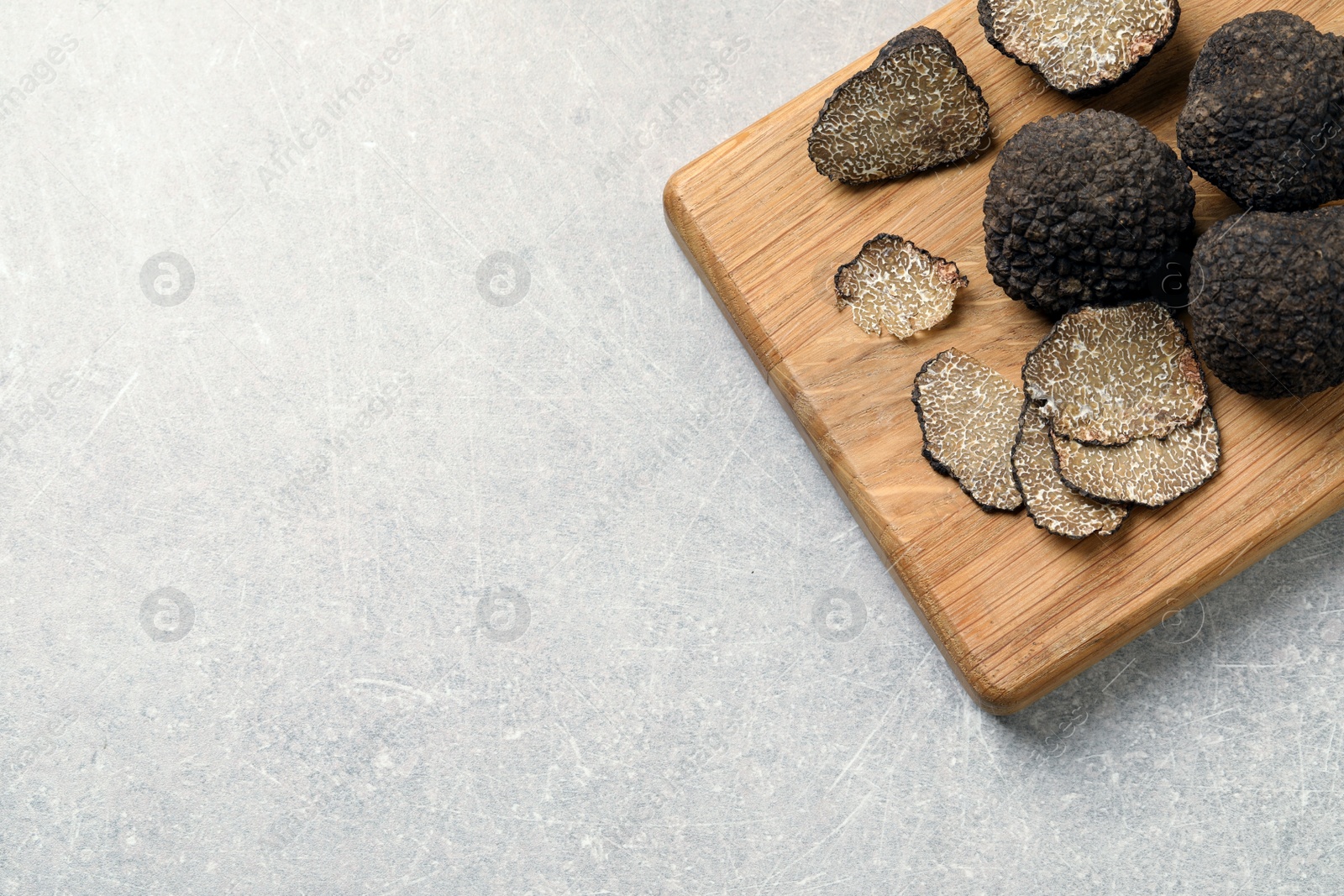 Photo of Black truffles with wooden board on light grey table, top view. Space for text