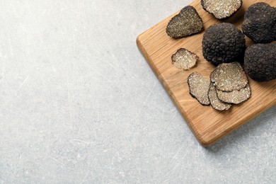 Black truffles with wooden board on light grey table, top view. Space for text