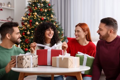 Photo of Christmas celebration in circle of friends. Happy woman opening gift at home