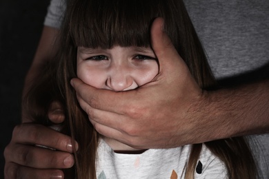 Photo of Adult man covering scared little girl's mouth, closeup. Child in danger