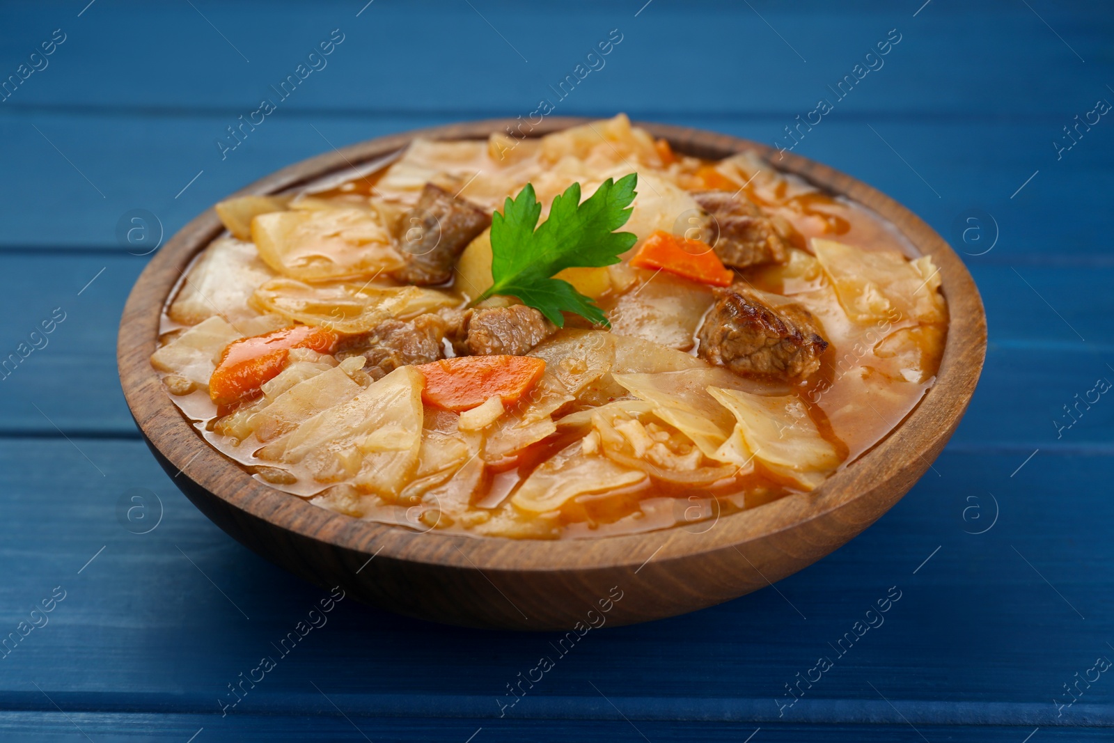 Photo of Tasty cabbage soup with meat, carrot and parsley on blue wooden table, closeup