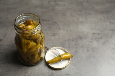 Glass jar with pickled peppers on grey table. Space for text