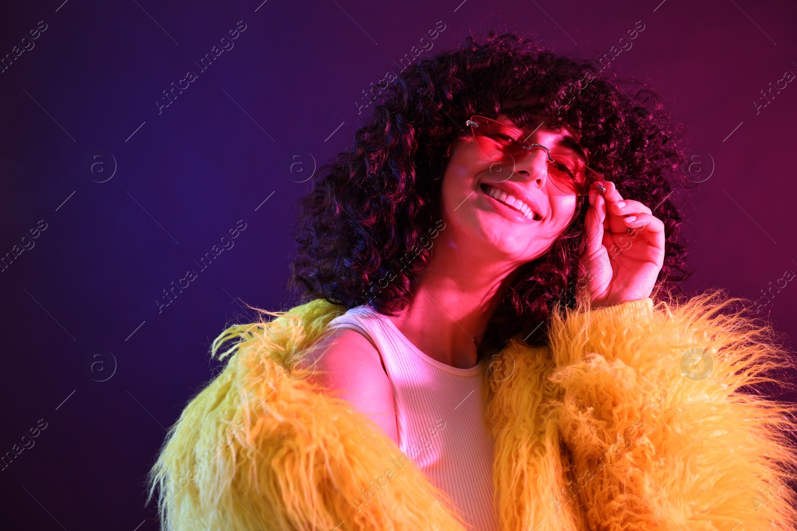 Photo of Beautiful young woman in yellow fur coat and sunglasses on color background in neon lights