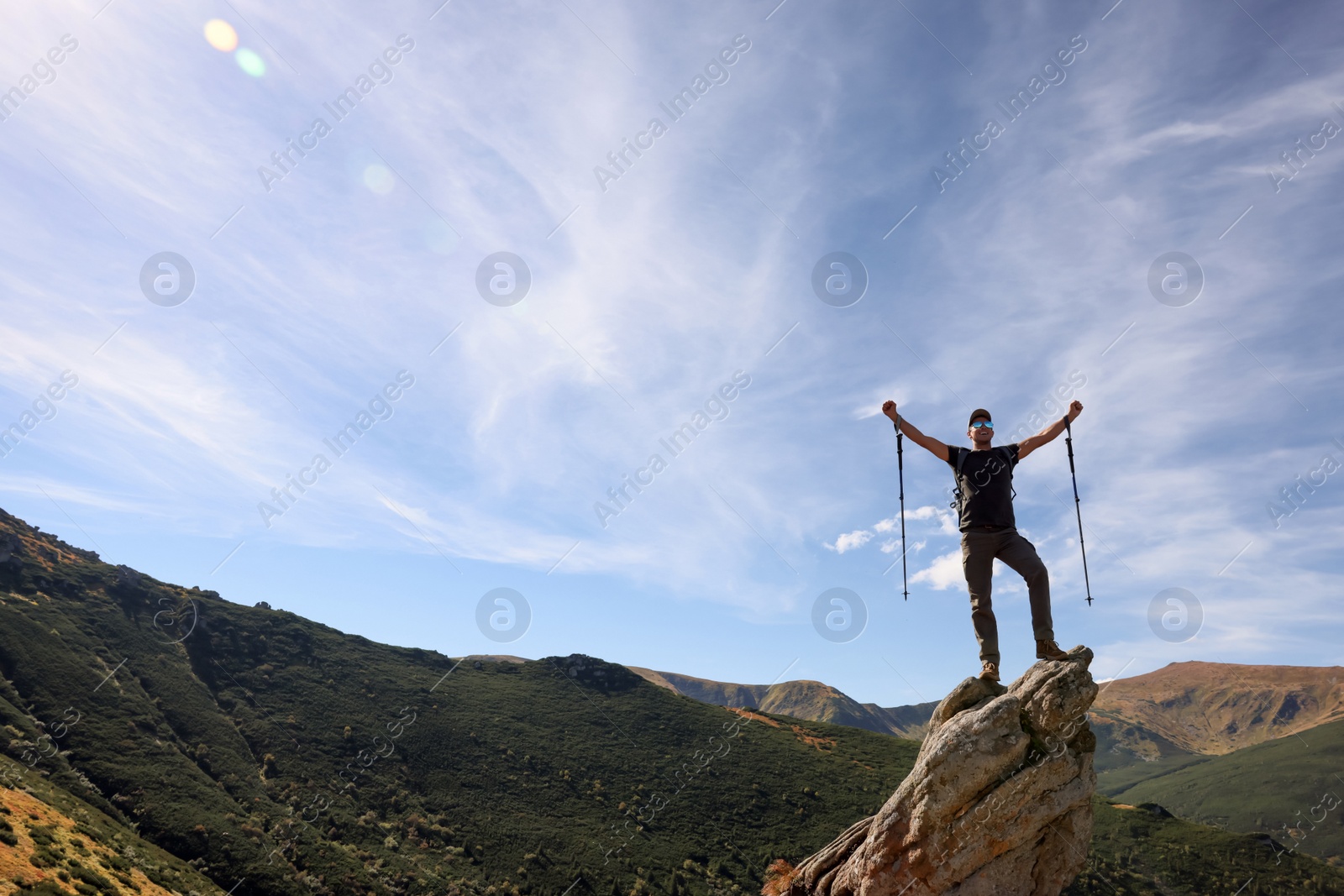 Photo of Man with backpack and trekking poles on rocky peak in mountains