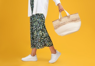 Photo of Young woman with stylish straw bag on yellow background, closeup