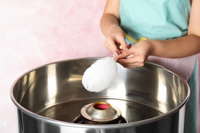 Photo of Young woman making cotton candy with modern machine on pink background, closeup