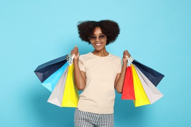 Photo of Happy African American woman in sunglasses with shopping bags on light blue background