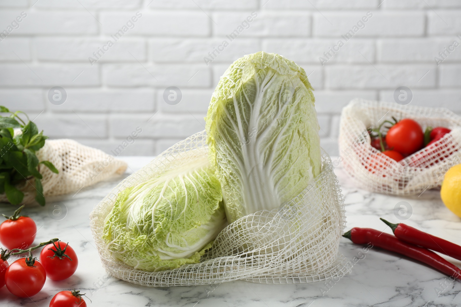 Photo of Fresh Chinese cabbages and other vegetables on white marble table near brick wall