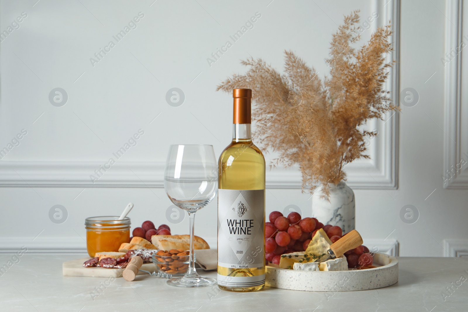 Photo of Bottle of white wine, glass and snacks on table