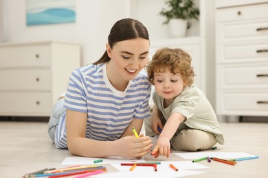 Photo of Mother and her little son drawing with colorful markers on floor at home