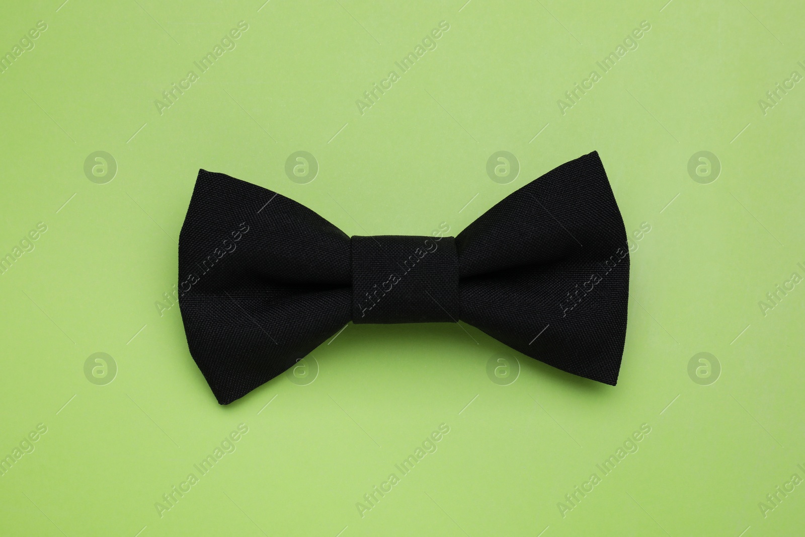 Photo of Stylish black bow tie on light green background, top view