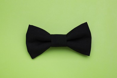 Stylish black bow tie on light green background, top view